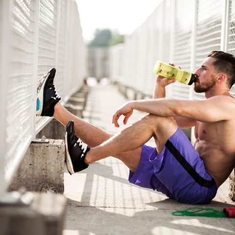 Mann der sich nach einem harten Training erholt und sitzend ein Sportgetränk zu sich nimmt für die Muskelregeneration