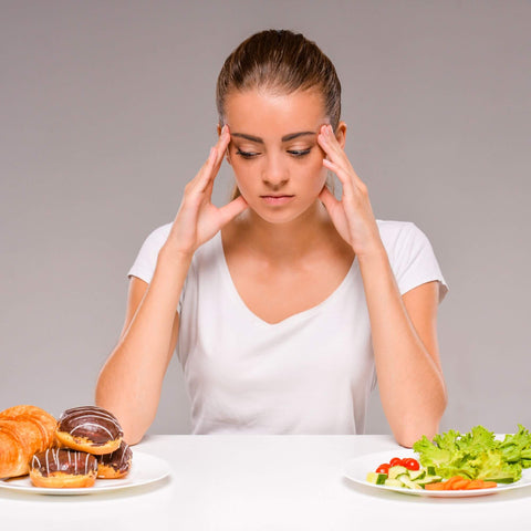 Frau die vor 2 verschiedenen Gerichten sitzt um die Problematik verschiedener Diäten aufzuzeigen