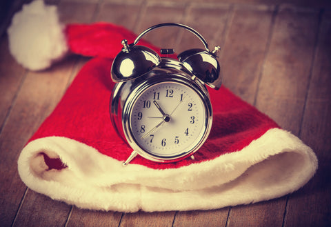 Old fashioned silver alarm clock placed on top of a Santa hat on a timber table