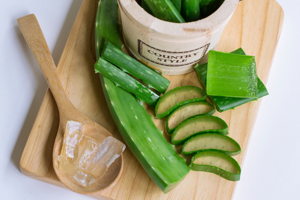 Aloe vera plant leaves, skin, and gel on wooden cutting board