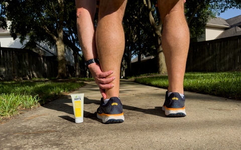 Man holding ankle while standing next to topical pain relief cream