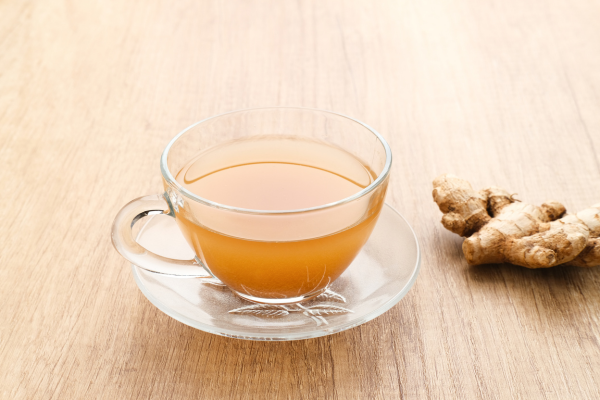 Glass cup of ginger tea next to ginger root