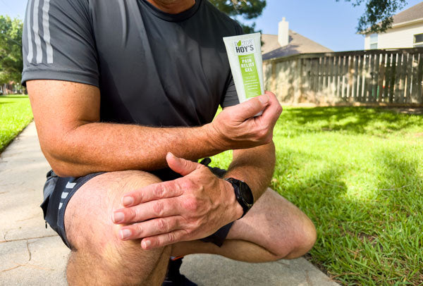 Man in athletic clothing outdoors applying pain relief gel to knee