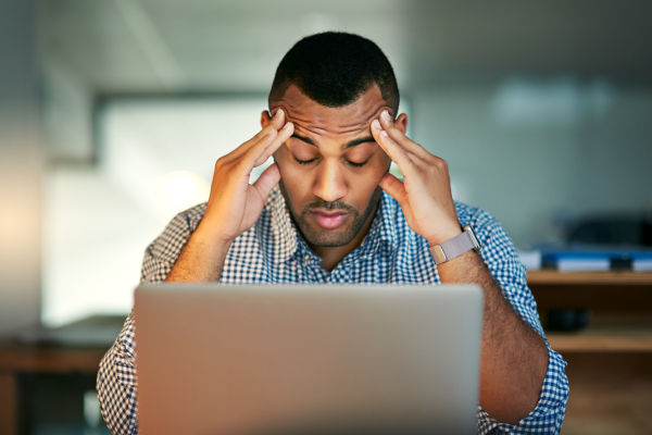 young businessman looking stressed and rubbing temples in front of computer