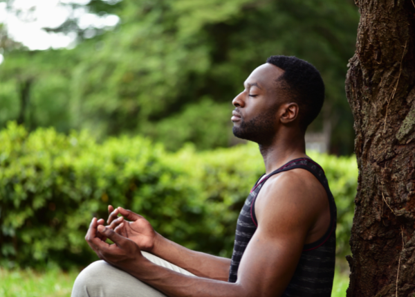 Man sitting outside by a tree while meditating