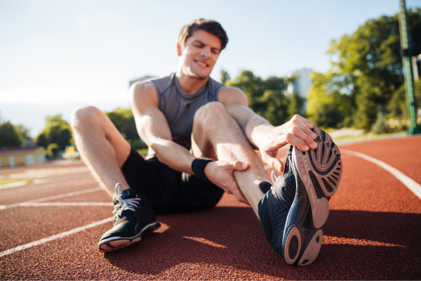Man on running track stretching leg and foot in pain