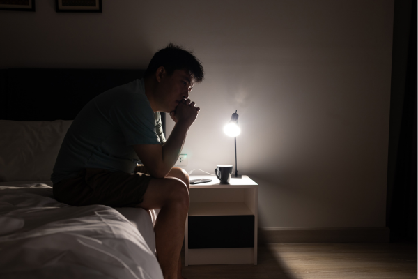 Man sitting on bedside in dark bedroom