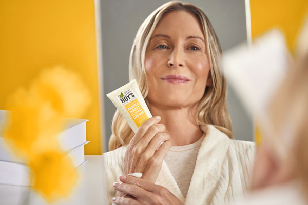 Woman smiling and looking in mirror while holding pain relief cream tube