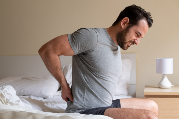 man with lower back pain sitting on edge of bed in morning