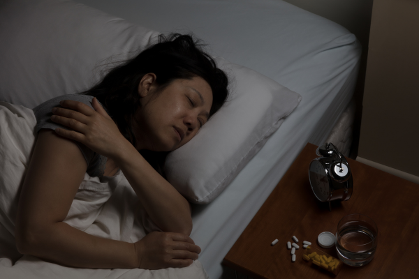 sleeping woman holding shoulder in bed next to pills