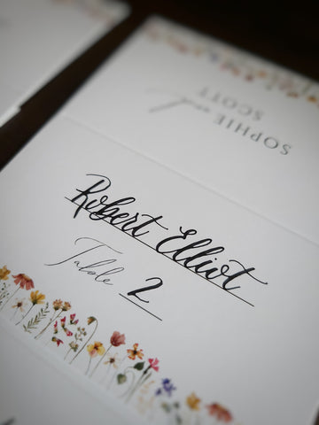 Escort cards with calligraphy detailing the first name, last name, and table number