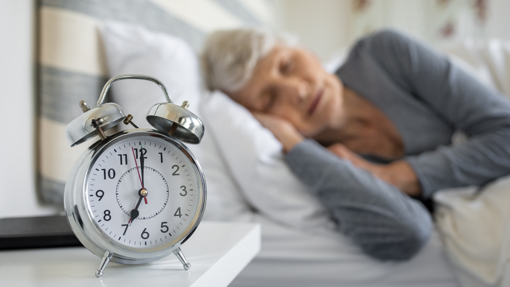 Older woman sleeping next to an alarm clock