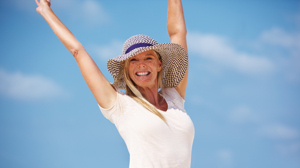 Happy woman in a sunhat raising her arms out of excitement in front of a clear, blue sky