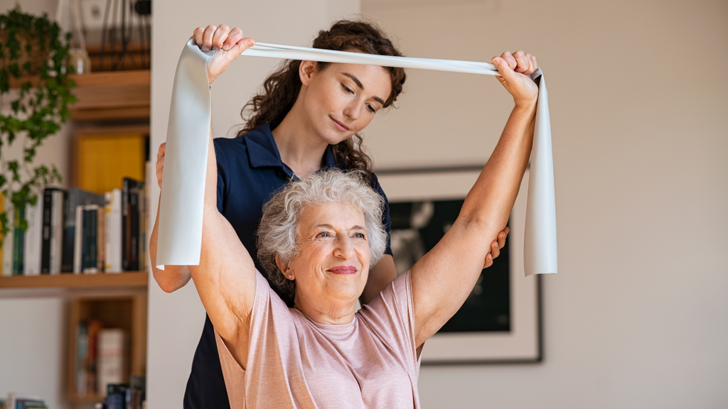 Older woman stretching her arms with a towel and her physical therapist is helping her