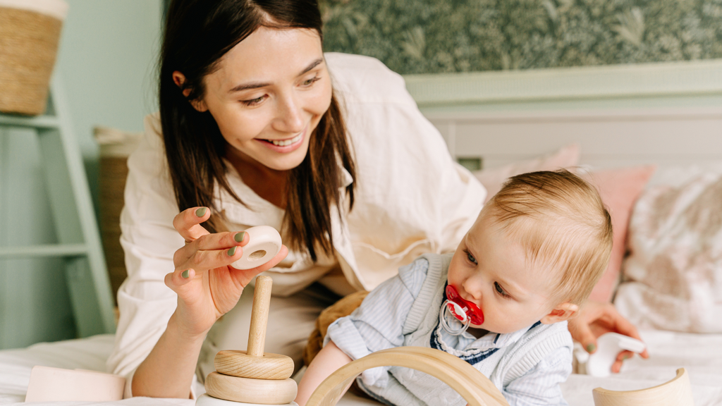 Woman showing her baby how to play with toy on the bed