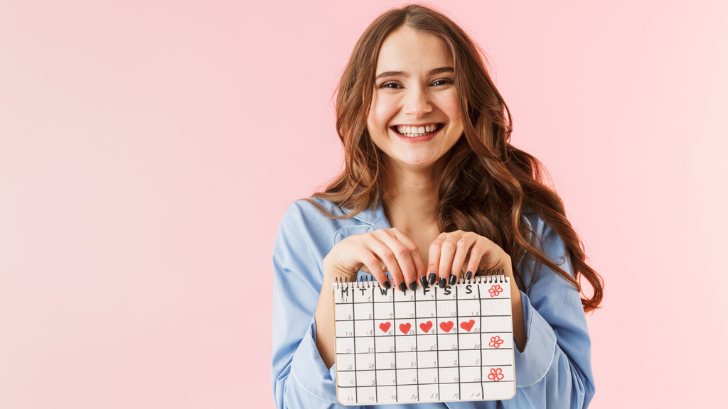 Teenage girl holding a calendar to track her PMS symptoms in front of a pink background