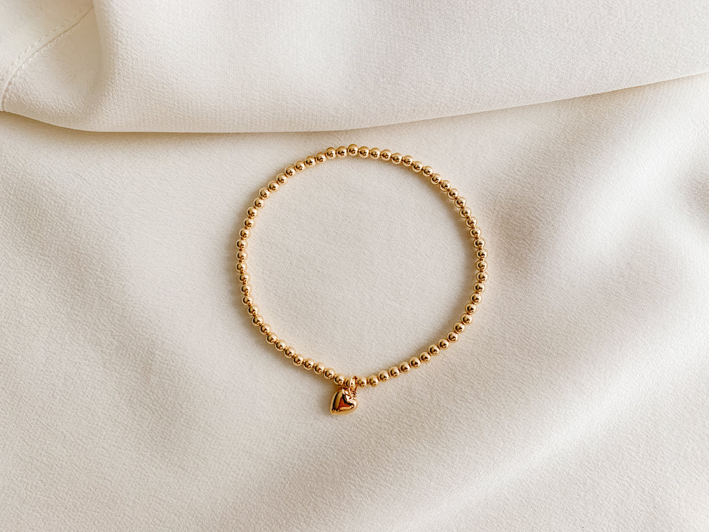 A gold bead bracelet in 14k gold filled metal with a tiny puffed heart charm.