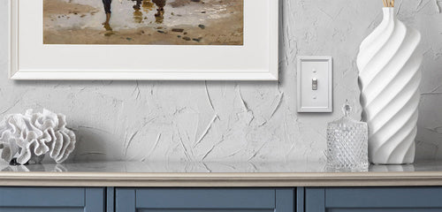 A photograph of the Shaker white metal wallplate on a white stucco wall, next to a painting, a white vase, and blue cabinetry, in a room decorated in a Coastal decor style