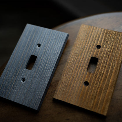 A close-up photograph of two Montana collection wood decorative wallplates with the rustic brown and rustic gray finish options