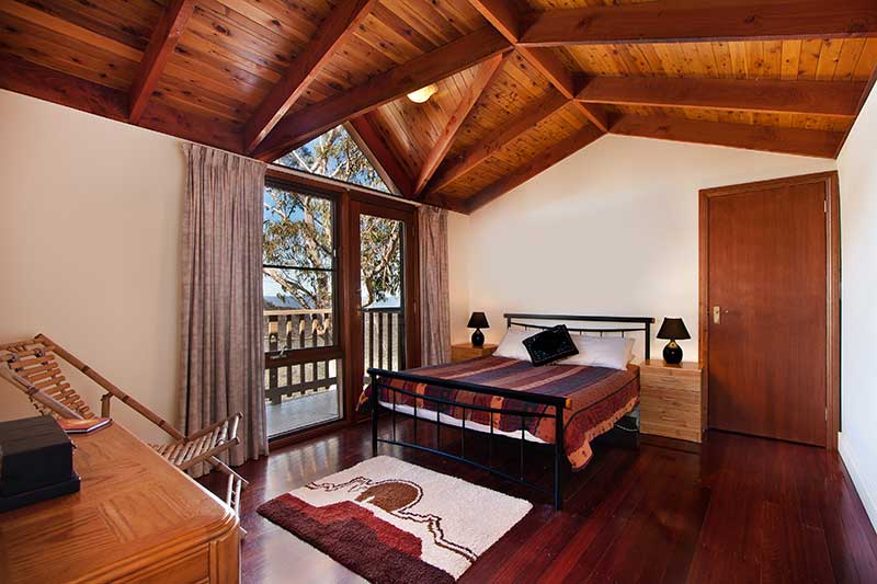 A Southwestern decor style bedroom with dark stained wood floors, stained wood ceilings, white walls, and a rug and bed spread with Southwestern inspired patterns and motifs