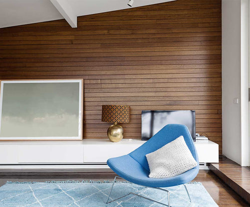 Professionally designed room with a Mid-Century Modern decor style, wood paneled walls, a blue rug, and a blue mid-century modern style lounge chair