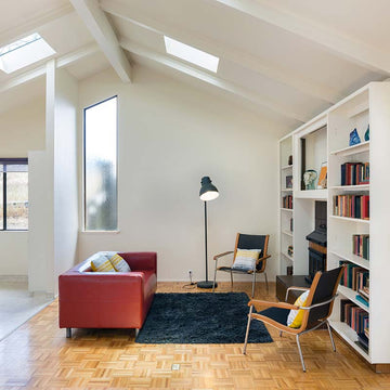 An interior photo of a professionally designed Mid-Century Modern decor style living room with white walls, a red couch, bookshelves, and mid-century modern style lounge chairs