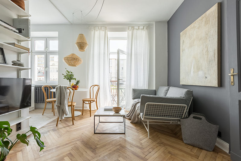 A Scandinavian decor style apartment with light wood floors, white and grey walls, an open door to a balcony, functional furniture, and a general hygge atmosphere