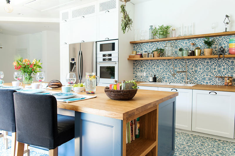 A Mediterranean decor style kitchen with blue island cabinetry, wood countertops, white walls, and blue and white mosaic tile floors and backsplashes