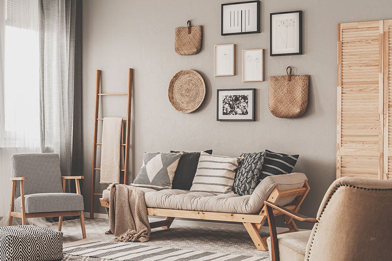 A Scandinavian decor style living room with wood furniture, a primarily beige color palette, an area rug, and numerous comfortable pillows on the couch