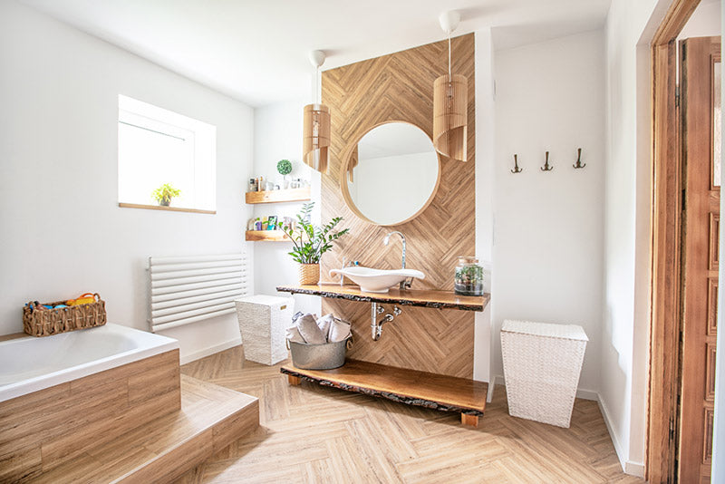 A Scandinavian decor style bathroom with white walls, natural light, exposed live edge wood countertops, light wood floors, wood drop down light covers, and a light wood backsplash that covers the entire wall