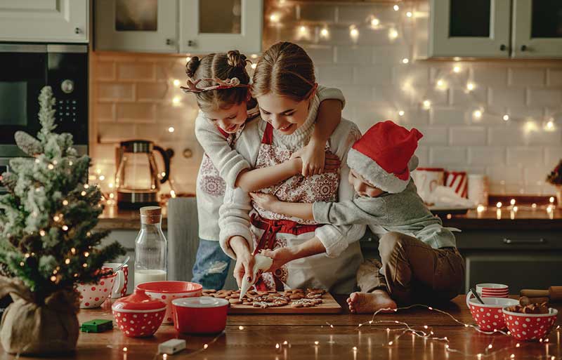 A woman smiling and making Christmas cookies with her two children in a large professionally designed kitchen