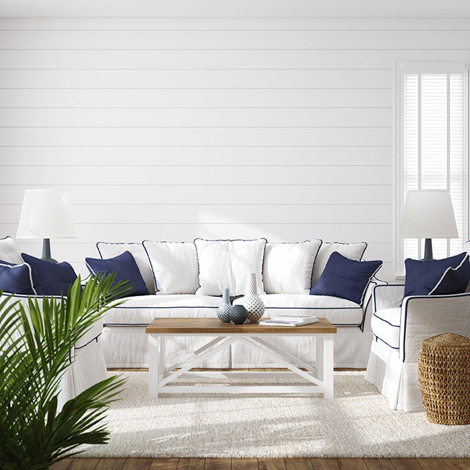 A Coastal decor style living room with white linen couches, navy blue pillows, white shiplap walls, and a white area rug