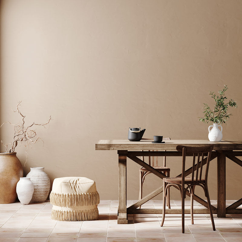 A Mediterranean decor style dinning room with a table made of wood, a green olive plant in a white vase on the table, beige walls, and tile floors