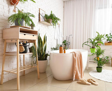 An interior photo of a professionally designed Scandinavian decor style bathroom with white brick walls, natural light, tan tile floors, a bathtub, and a lot of green plants