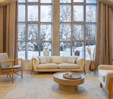 An interior photo of a professionally designed Modern Mountain decor style living room with a light neutral color palette, a large oversized window with large amounts of natural light, heavy beige window drapes, and light and weathered wood design elements