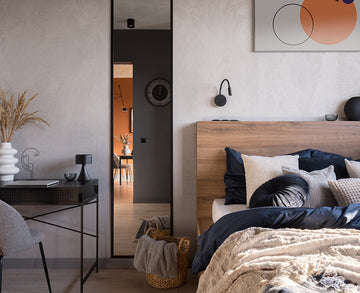 An interior photo of a professionally designed Eclectic decor style bedroom with blended aspects of Modern and Bohemian styles, a bed, gray walls, an orange abstract painting on the wall, and the orange-painted kitchen shown in the reflection of a mirror