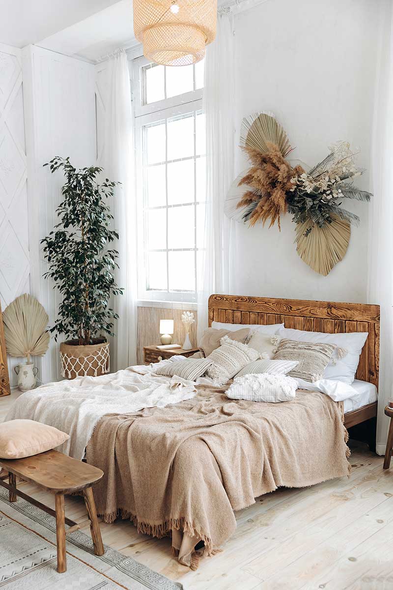 Photo of a Bohemian decor style bedroom with wood floors, white walls, a woven ceiling light cover, plants, natural light, and textured bedding