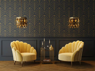 An interior photo of a professionally designed Art Deco decor style lounging area with yellow upholstered chairs, gold light fixtures, a gold coffee table, and dark walls with gold geometric patterned wallpaper