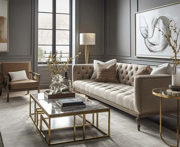 An interior photo of a professionally designed Transitional decor style living room with a neutral color palette, large windows, brass metal tables, a white rug, and a Traditional style couch