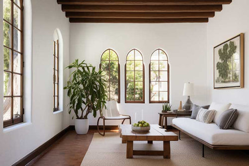 A sunroom in a spanish colonial home that has white walls, exposed wood ceiling beams, warm weather plants, wood furniture, and rounded windows