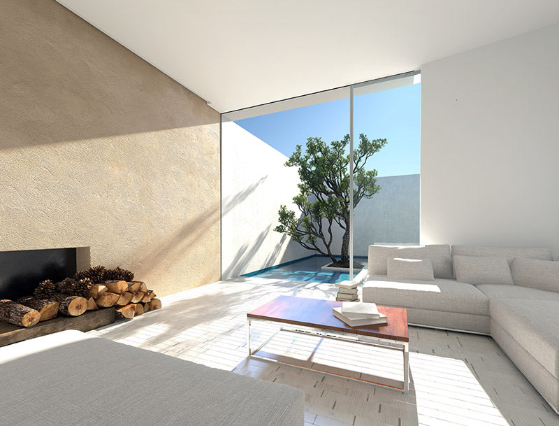 An indoor-outdoor lounging room with a wall that opens directly to the outdoors, white fabrics lounging couches, a fireplace with wood stacked in front of it, and white tile floors, with lot of natural sunlight