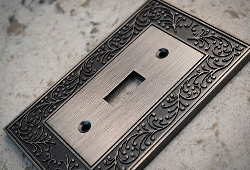 A photograph of the English Garden antique nickel wallplate laying on a granite countertop