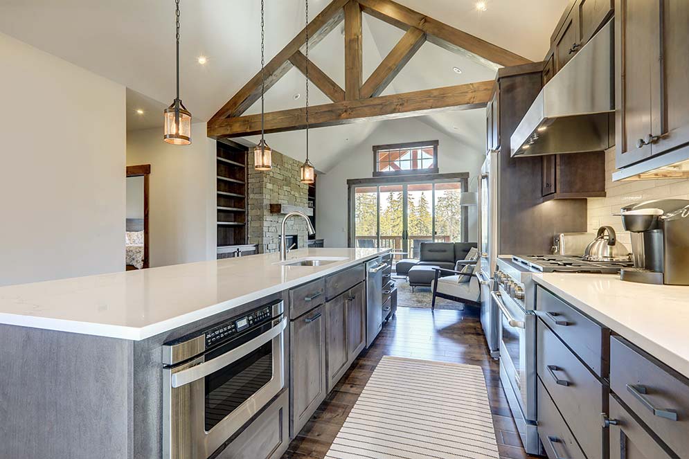 Professionally designed kitchen with a Modern Mountain decor style, large wood exposed beams, large windows, stainless steel appliances, and hardwood floors