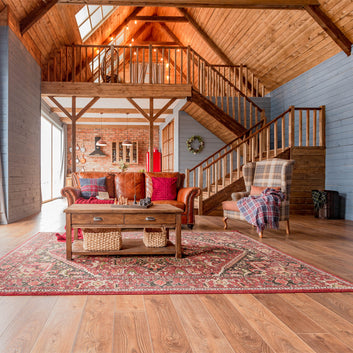 An interior photo of a professionally designed Rustic Lodge Cabin decor style living room and loft with wood furniture and accents, a large rug, and a leather couch