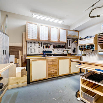 An interior photo of a professionally designed Workshop Garage decor style room with good lighting, wood shelving, tools hanging on a pegboard, white walls, and a cement floor