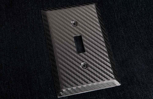 A close-up photograph of the black Carbon Fiber wallplate collection on a black cloth backdrop