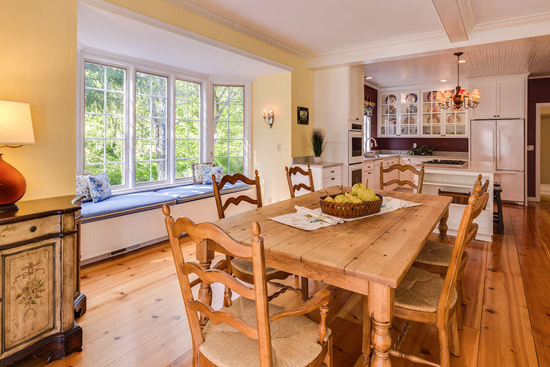 An interior photo of a professionally designed Country decor style dining room and kitchen with a large window, wood table, and wood floors