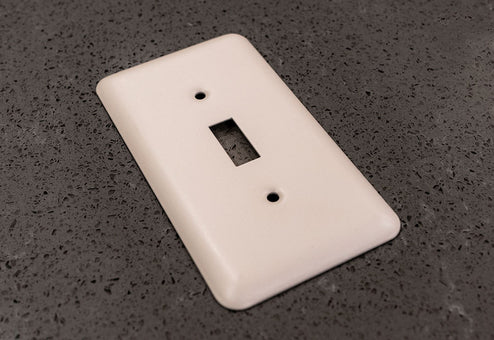 A photo of the Devon off-white decorative metal wallplate on a granite countertop