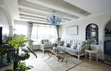 An interior photo of a professionally designed Mediterranean decor style living room with a blue and white color palette, large windows providing natural light, green plants, tile floors, blue metal fixtures, and neutral color painted walls