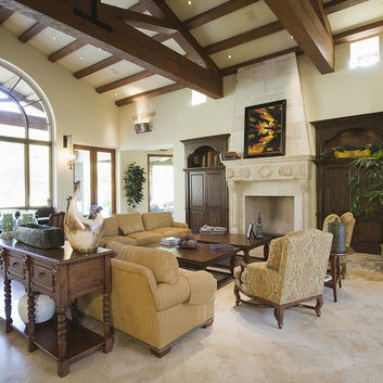 An interior photo of a professionally designed Mediterranean decor style living room with a large window, exposed wood beams, a fireplace, wood furniture, and a beige color palette